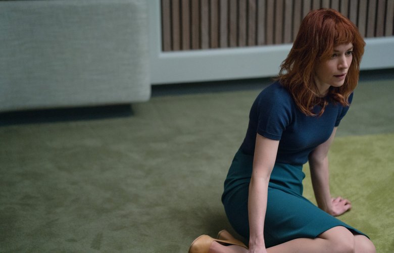 一个红头发的女人，穿着蓝色衬衫和配套的裙子，坐在铺着地毯的办公室会议室地板上;《遣散费》剧照