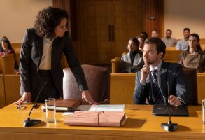 一个留着棕色短发卷发的女人站在桌旁，对坐在她旁边的一个男人说话，两人在法庭上都穿着西装;《女绿巨人:律师》剧照