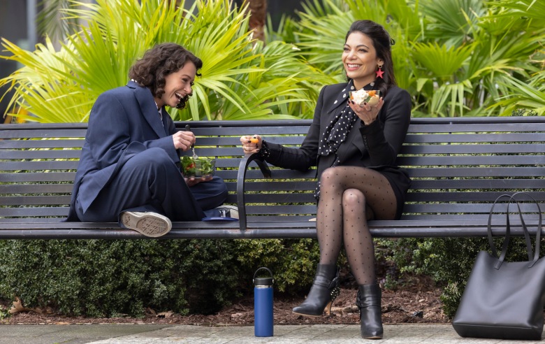 两个女人坐在明亮的绿色树叶前的长凳上，其中一个穿着一件超大的西装，盘腿坐着，另一个穿着皮夹克和靴子，双腿交叉;《女绿巨人》剧照