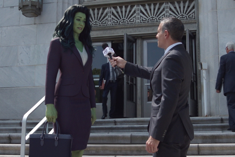 一位身材高挑、皮肤碧绿、穿着紫色西装的女律师站在法院外的台阶上，拿着麦克风对记者讲话;《女绿巨人:律师》剧照